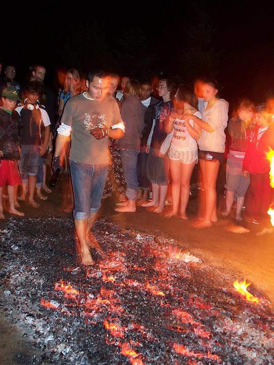 Young person firewalking barefoot across glowing hot coals while the community watches